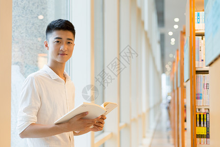 毕业男站在图书馆书架旁看书的帅气男高中生同学背景