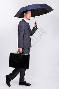 男人撑伞提着公文包撑伞走路的商务人士背景