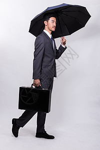 提着东西男人提着公文包撑伞走路的商务人士背景