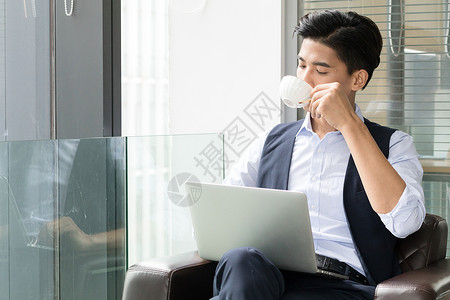 年轻商务男士落地窗前喝咖啡背景图片