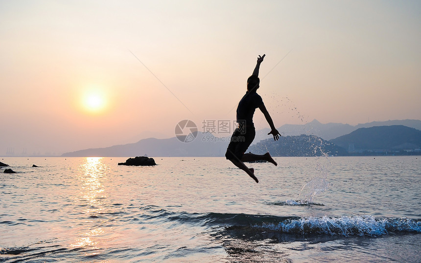 夕阳下海边跃起的舞者剪影图片