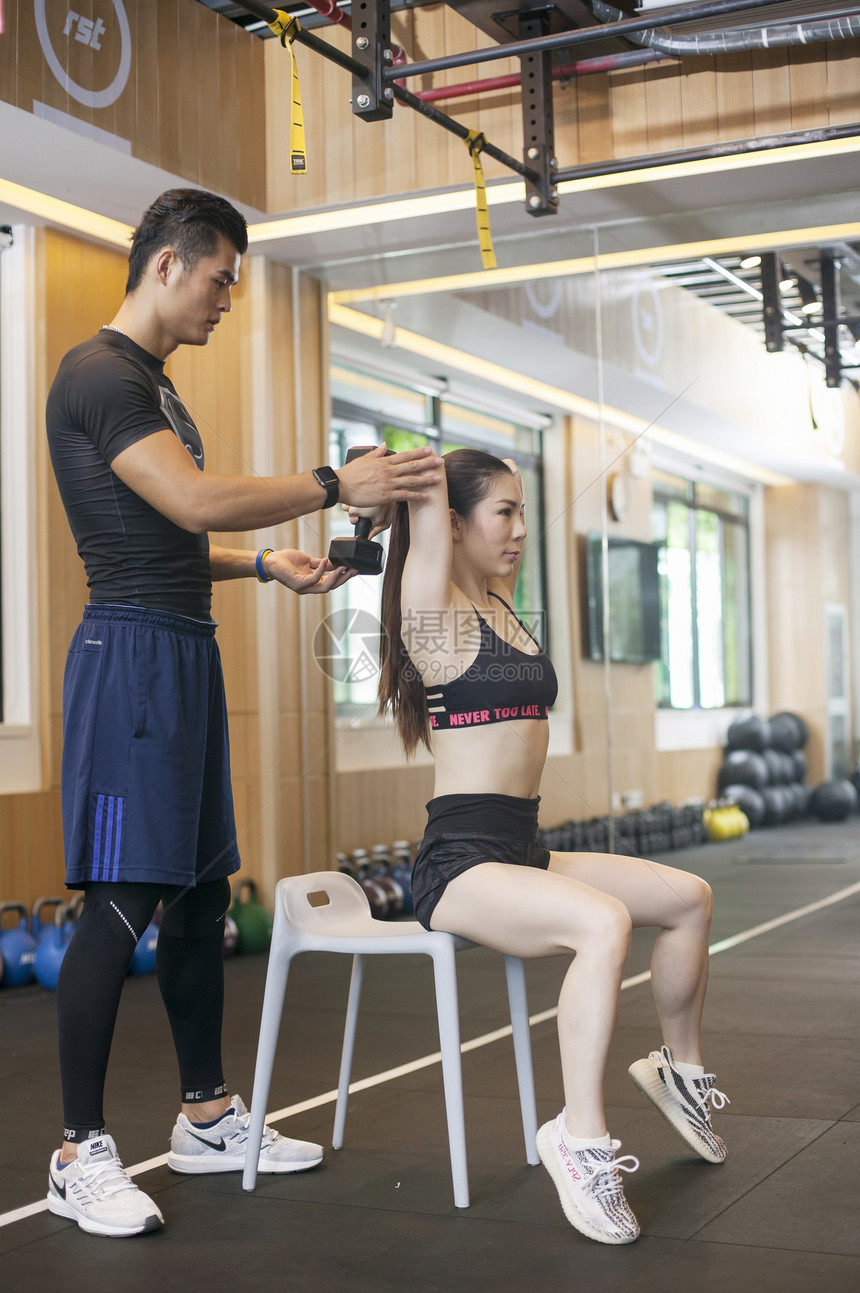 男教练在健身房给女性练习力量图片