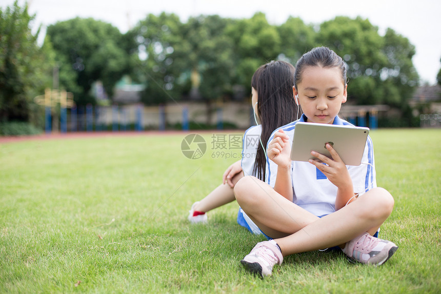 坐在草坪上使用平板电脑的小学生图片