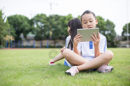 线上听课坐在草坪上使用平板电脑的小学生背景