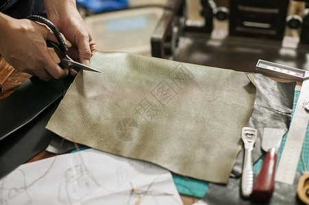 制作皮具皮匠在专注的裁剪皮革背景