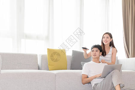 年轻夫妻一起在客厅沙发上看电视背景图片