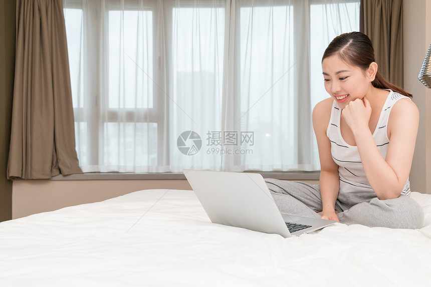 坐在床上玩电脑休闲放松的年轻女性图片