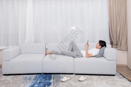 男生躺在沙发上玩手机购物图片