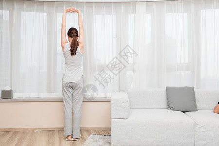 年轻女性在客厅窗前伸展运动高清图片