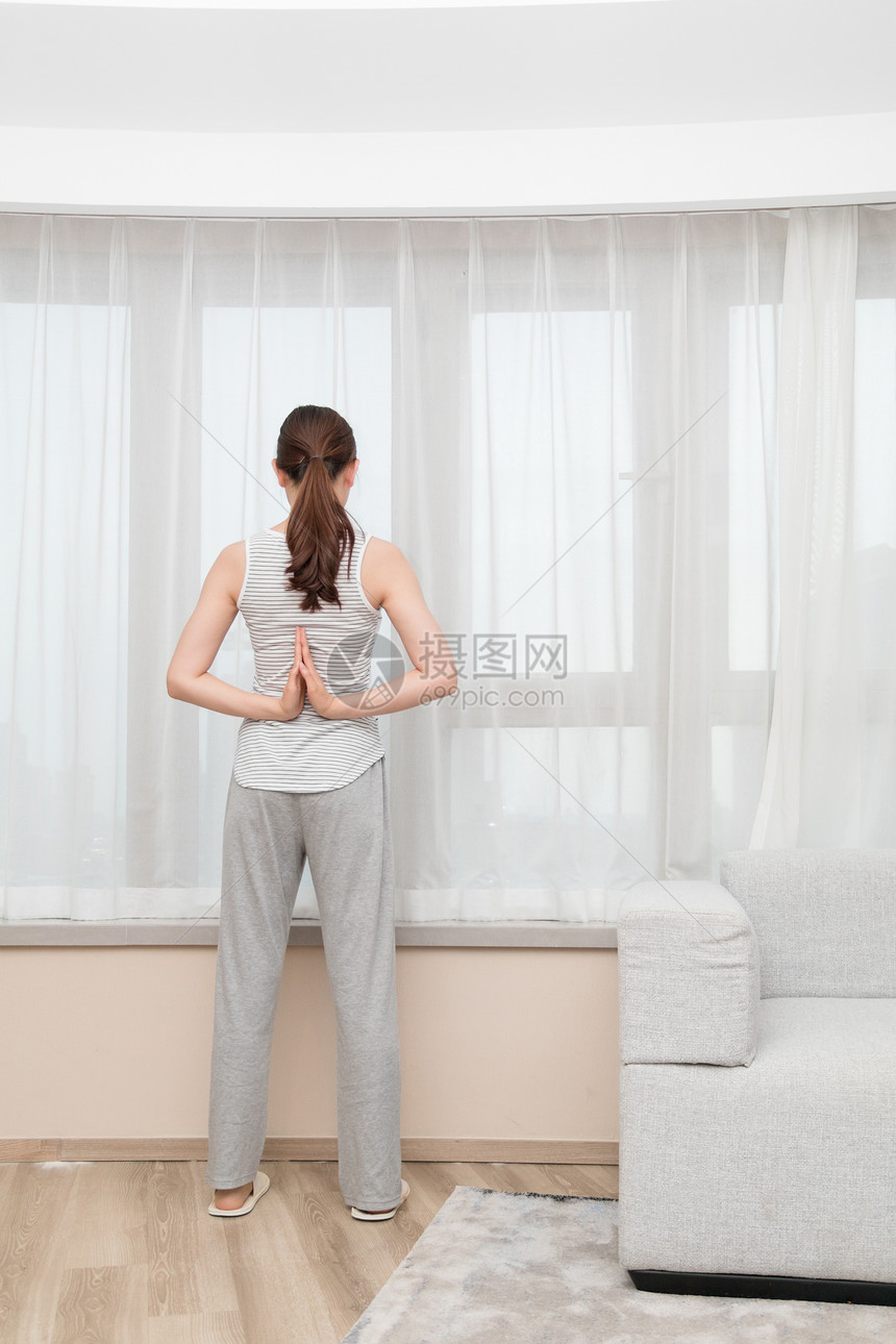 年轻女性在客厅窗前伸展运动图片