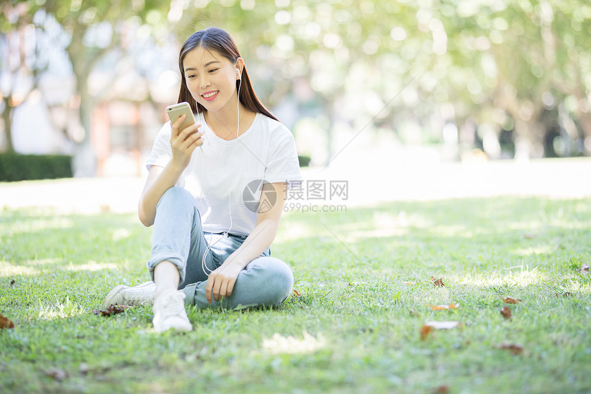 校园草坪上看手机听音乐的女生图片