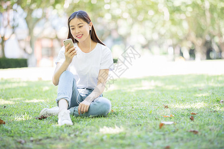 校园草坪上看手机听音乐的女生图片