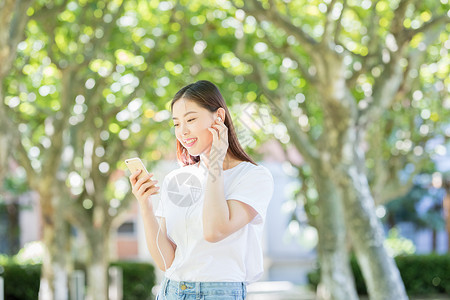 树下用手机听音乐的甜美女生背景图片