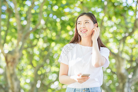 树下用手机听音乐的甜美女生高清图片