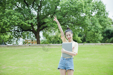 手抱电脑校园草地前女生抱着电脑背景