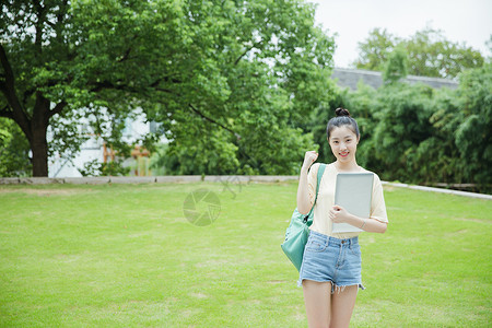 女生抱花校园草地前女生抱着电脑背景