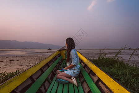 公园木船湖面上欣赏日落的美丽女孩背景