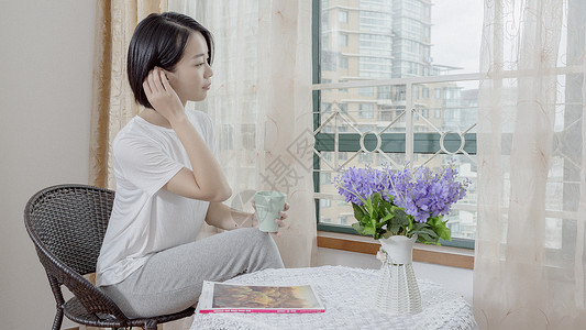 女子在窗边手持水杯休息高清图片