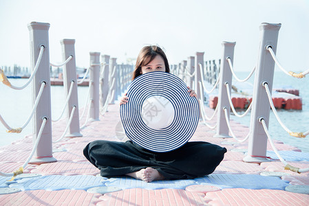 海边栏杆海边渔港旁坐着拿着草帽的女模特背景