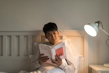 晚上坐在床头看书的年轻男性图片
