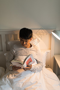 晚上床头晚上坐在床头看书的年轻男性背景