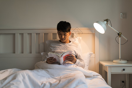 晚上坐在床头看书的年轻男性高清图片