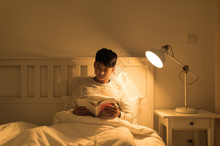 看书晚上晚上坐在床头看书的年轻男性背景