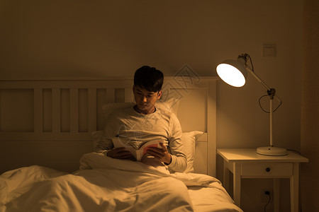 晚上床头晚上坐在床头看书的年轻男性背景