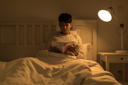 晚上坐在床头看书的年轻男性高清图片