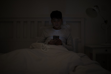 晚上玩游戏睡前坐在床上玩手机的男子背景