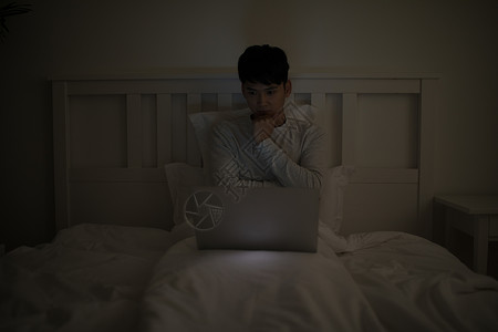 睡前坐在床上玩电脑打电脑的男子图片