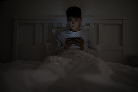 睡吧睡前坐在床上玩手机的男子背景