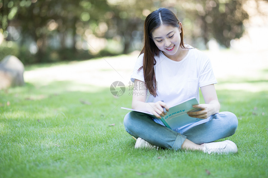 拿着课本坐在草坪上看书的大学生图片