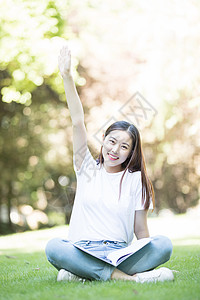 愉快地坐在草坪上学习的女同学背景