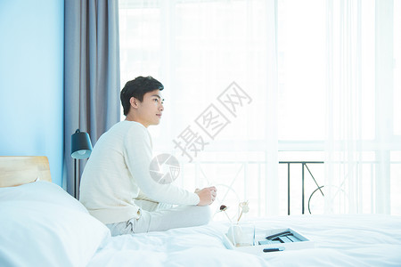 卧室里坐在床边的年轻男性背景图片