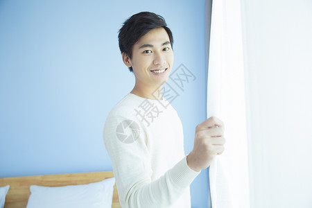 卧室里拉窗帘的年轻男性背景图片
