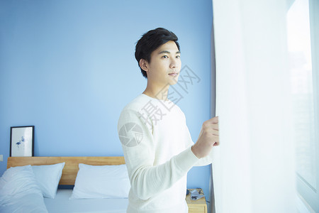 卧室里拉窗帘的年轻男性图片