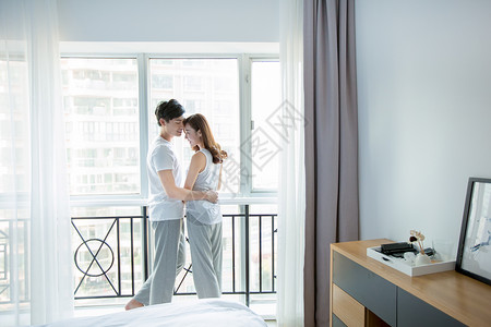 卧室窗边年轻情侣在窗边拥抱背景