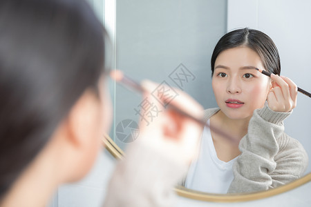 站在镜子前画眉的年轻女性图片