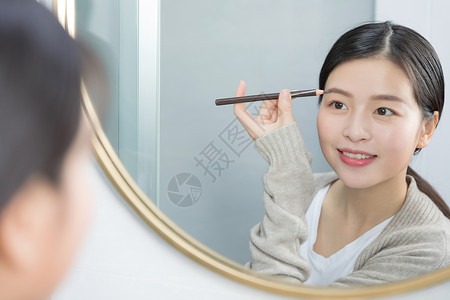 站在镜子前画眉的年轻女性高清图片