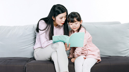 坐在沙发上的妈妈妈妈和女儿坐在沙发上看书背景