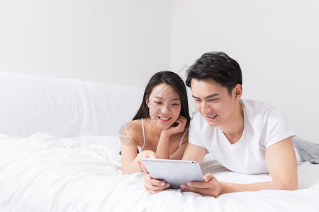 年轻夫妻床上开心看平板背景图片