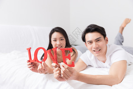 年轻夫妻开心躺床上手拿LOVE高清图片