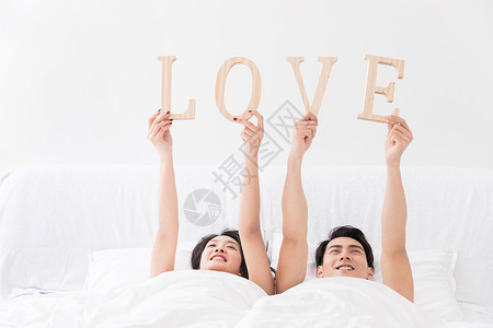 木制模特年轻夫妻躺床上手拿LOVE背景