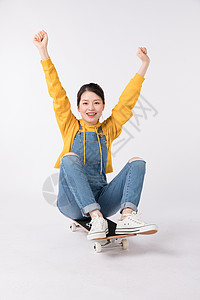清纯滑板女生坐在滑板上欢呼的年轻女生背景
