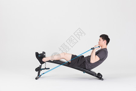 杠铃板坐在运动器械上拉阻力带的健身男性背景