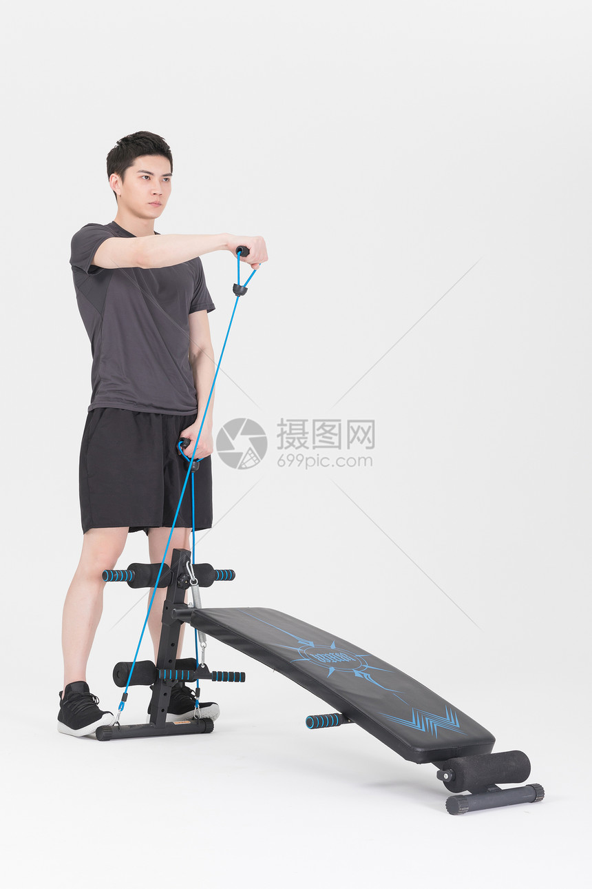 站在仰卧板旁拉阻力带的健身男性图片