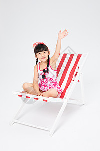 坐在沙滩椅上的女孩沙滩椅上的挥手的泳装小女孩背景