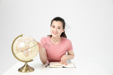 青年女性学生课桌上看地球仪背景图片