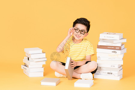 拿着书本坐在书旁的快乐男孩高清图片